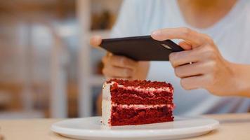 bloguera asiática amigable mujer influyente come pastel en el café de la noche. hermosa jovencita feliz relajarse diversión usando tecnología teléfono móvil tomando una foto de su carga de comida en las redes sociales en el campus universitario.