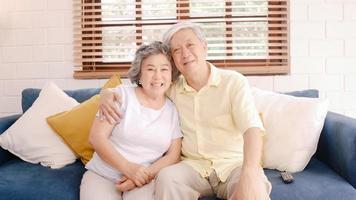 Asian elderly couple watching television in living room at home, sweet couple enjoy love moment while lying on the sofa when relaxed at home. Enjoying time lifestyle senior family at home concept. photo