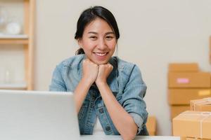 Business woman feeling happy smiling and looking to camera while working in her office at home. Beautiful Asian young entrepreneur owner of SME with small business owner at home office concept. photo
