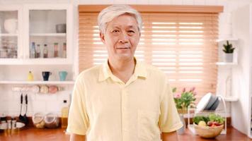un anciano asiático que se siente feliz sonriendo y mirando a la cámara mientras se relaja en la cocina de casa. estilo de vida de los hombres mayores en el concepto de hogar. foto