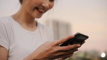 Cheerful Asian tourist blogger woman using touchscreen technology at smartphone while walking on the street at downtown city in the evening. Lifestyle backpack tourist travel holiday concept. photo