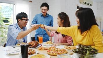 Happy young friends group having lunch at home. Asia family party eating pizza food and laughing enjoying meal while sitting at dining table together at house. Celebration holiday and togetherness. photo