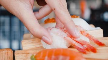 Asian woman eating sushi in japanese restaurant, young female holding chopsticks and eating shrimp sushi in lunch time in summer. Lifestyle women eating traditional food concept. photo