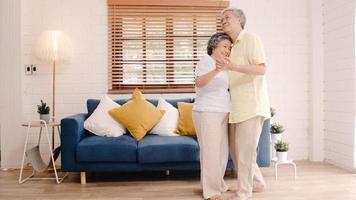 Asian elderly couple dancing together while listen to music in living room at home, sweet couple enjoy love moment while having fun when relaxed at home. Lifestyle senior family relax at home concept. photo