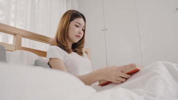 Beautiful attractive young Asian woman reading a book while lying on the bed when relax in her bedroom at home in the morning. Lifestyle women using relax time at home concept. photo
