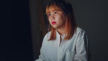 Young asian woman working late using desktop on desk in living room at home. Asia business woman writing notebook document finance and calculator in night at home office. Overworked female concept. photo