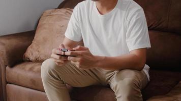 joven asiático usando joystick jugando videojuegos en la televisión en la sala de estar, el hombre se siente feliz usando el tiempo de relajación acostado en el sofá en casa. los hombres juegan y se relajan en el concepto de hogar. foto