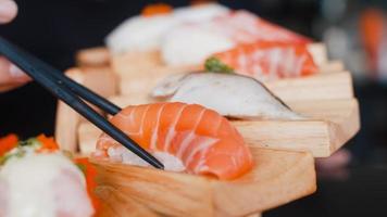 mujer asiática comiendo sushi en un restaurante japonés, mujer joven sosteniendo palillos y comiendo sushi de salmón a la hora del almuerzo en verano. mujeres de estilo de vida que comen el concepto de comida tradicional.
