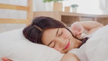 Beautiful attractive young Asian woman wake up, smiling and stretching her arms in her bed in bedroom. Young asia female use relax time at home. Lifestyle women relax at home concept. photo