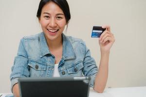 hermosa mujer asiática de negocios inteligente que usa una tableta para comprar compras en línea con tarjeta de crédito mientras usa una elegante ropa informal sentada en el escritorio en la sala de estar en casa. mujer de estilo de vida que trabaja en el concepto de hogar. foto