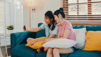 Young Lesbian lgbtq women couple selfie at home. Asian lover female happy relax fun using technology mobile phone smiling take a photo together while lying sofa in living room concept.