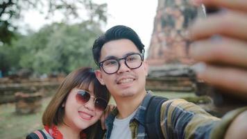 Traveler Asian couple using smartphone taking selfie while spending holiday trip at Ayutthaya, Thailand, Couple enjoy their journey at amazing landmark in traditional city. photo