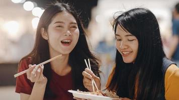 Asian young women friends travel in Bangkok, Thailand, beautiful female feeling happy walking and eating Pad Thai at The Khao San Road. Women travel eat street food in Thailand concept. photo