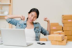 Smart Asian young entrepreneur business woman owner of SME working and relax raise arm up and close eye in front of laptop computer on desk at home. Small business owner at home office concept. photo