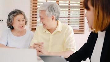 Asia smart female agent offers health insurance for elderly couples by document, tablet and laptop. Aged Asian couple consulting with insurance agent while sitting together with at home. photo