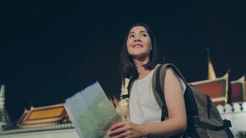 Backpacker Asian woman travel in Bangkok, Thailand. Young Asian tourist girl looking maps for direction places at night while walk along the street enjoying the journey holiday travel concept. photo