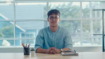 joven creativo asiático sonriendo en la oficina. hombre de negocios feliz relajarse después del trabajo, mirando a la cámara, situación de negocios en el concepto de lugar de trabajo moderno. foto