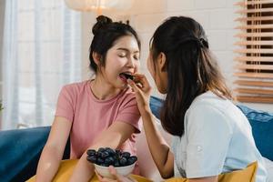 Asian Lesbian lgbtq women couple eat healthy food at home, Young Asia lover female feeling happy feeding grape together while lying sofa in living room at home in the morning concept.