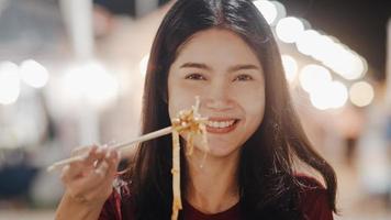 Asian young woman travel in Bangkok, Thailand, beautiful female feeling happy walking and eating Pad Thai at The Khao San Road. Women travel eat street food in Thailand concept. photo