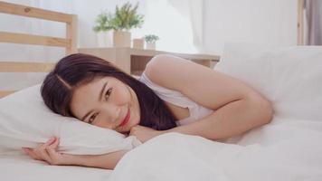 mujer asiática sonriendo acostada en la cama en el dormitorio, hermosa mujer japonesa usando tiempo de relajación después de despertarse en casa. mujeres de estilo de vida que usan el concepto de tiempo de relajación en casa. foto