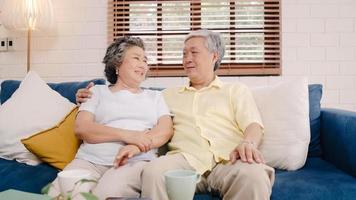 Asian elderly couple feeling happy smiling and looking to camera while relax on the sofa in living room at home. Enjoying time lifestyle senior family at home concept. Portrait looking at camera. photo