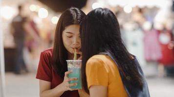 Asian young women friends travel in Bangkok, Thailand, beautiful female feeling happy drinking cocktail at The Khao San Road. Women travel eat street food in Thailand concept.