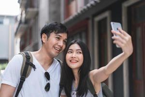 Asian blogger couple travel in Beijing, China, sweet couple using mobile phone selfie photo view while spending sweet time in holiday trip. Couple travel in city concept.