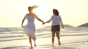 Young Asian lesbian couple running on beach. Beautiful women friends happy relax having fun on beach near sea when sunset in evening. Lifestyle lesbian couple travel on beach concept. photo