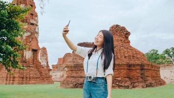 Young Asian backpacker blogger woman casual take selfie video call on mobile phone sharing live online for audience travel together at pagoda old city, Lifestyle tourist travel holiday concept. photo
