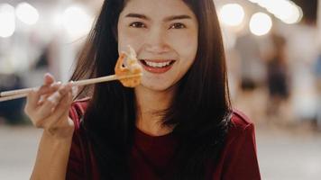 mujer joven asiática viaja en bangkok, tailandia, hermosa mujer que se siente feliz caminando y comiendo pad thai en la calle khao san. las mujeres viajan comen comida callejera en el concepto de tailandia. foto