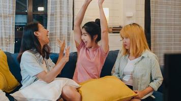 Group of Asian women couple play games at home, female using joystick having funny moment together on sofa in living room in night. Teenager young friend football fan, celebrate holiday concept. photo