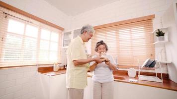 Asian elderly couple man holding cake celebrating wife's birthday in kitchen at home. Chinese couple enjoy love moment together at home. Lifestyle senior family at home concept. photo