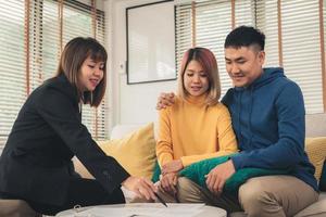 Happy young Asian couple and realtor agent. Cheerful young man signing some documents while sitting at desk together with his wife. Buying new house real estate. Signing good condition contract. photo