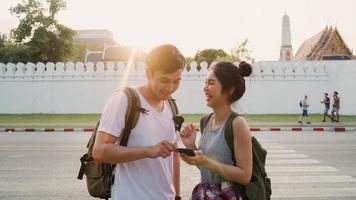 Traveler Asian couple direction on location map in Bangkok, Thailand, sweet couple using mobile phone looking on map while spending holiday trip in sunset. Lifestyle couple travel in city concept. photo