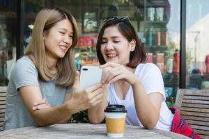 Cheerful asian young women sitting in cafe drinking coffee with friends and talking together. Attractive asian woman enjoying coffee while using smartphone for talking, reading and texting. photo