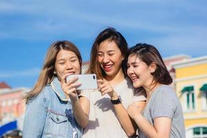 Attractive beautiful asian friends women using a smartphone. Happy young asian teenage at urban city while taking self portraits with her friends together with a smartphone. photo