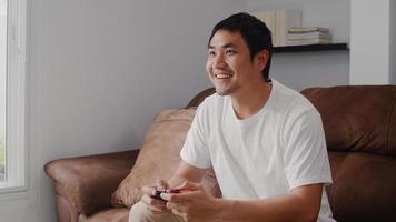 Young Asian man using joystick playing video games in television in living room, male feeling happy using relax time lying on sofa at home. Men play games relax at home concept. photo