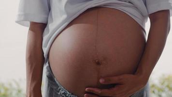 joven asiática embarazada sosteniendo su vientre hablando con su hijo. mamá se siente feliz sonriendo positiva y pacífica mientras cuida al bebé, el embarazo cerca de la ventana en la sala de estar en el concepto de hogar. foto