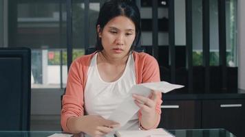 Young Asian Pregnant woman records of income and expenses at home. Mom worried, serious, stress while record budget, tax, financial document working in living room at home concept. photo