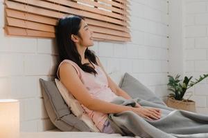 Asian Japanese woman wakes up at home. Young Asian girl feeling happy relax rest smile after sleep all night lying on bed, feel comfortable and calm in bedroom at home in the morning. photo