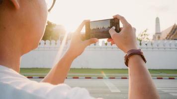 hombre asiático viajero que usa un teléfono móvil para tomar una foto mientras pasa un viaje de vacaciones en bangkok, tailandia, el hombre disfruta del viaje en un punto de referencia increíble al atardecer. los hombres de estilo de vida viajan en concepto de ciudad.