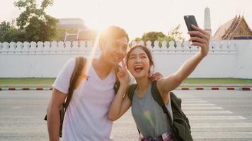 Asian blogger couple travel in Bangkok, Thailand, sweet couple using mobile phone selfie and photo view while spending sweet time in holiday trip in sunset. Couple travel in city concept.