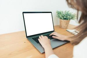 Young Asian woman working using and typing on laptop with mock up blank white screen while at home in office work space. Businesswoman working from home via portable computer. Enjoying time at home. photo