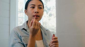 Beautiful Asian woman using lipstick make up in front mirror, Happy Chinese female using beauty cosmetics to improve herself ready to working in bathroom at home. Lifestyle women relax at home concept