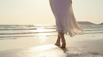 joven mujer asiática caminando en la playa. hermosa mujer feliz relajarse caminando en la playa cerca del mar al atardecer en la noche. las mujeres de estilo de vida viajan en concepto de playa. foto