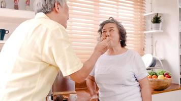 Asian elderly couple having breakfast in the kitchen at home. Chinese sweet couple man feeding cookies to his wife at home. Lifestyle senior family at home concept. photo