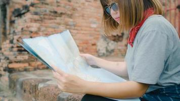 viajero mujer asiática dirección y mirando en el mapa de ubicación mientras pasa un viaje de vacaciones en ayutthaya, tailandia, mujer mochilero disfruta del viaje en la ciudad tradicional. concepto de viaje de las mujeres de estilo de vida. foto