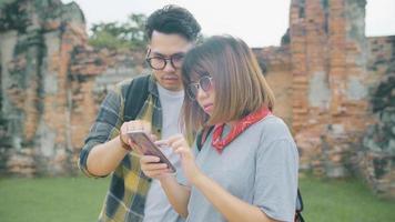 Traveler Asian couple using smartphone for direction and looking on location map while spending holiday trip at Ayutthaya, Thailand, backpacker sweet couple enjoy journey in traditional city. photo