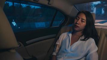 Successful young Asia businesswoman in fashion office clothes sleeping sitting on passenger back seat of car in urban modern city in night. People occupational burnout syndrome concept. photo