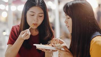 Asian young women friends travel in Bangkok, Thailand, beautiful female feeling happy walking and eating Pad Thai at The Khao San Road. Women travel eat street food in Thailand concept. photo